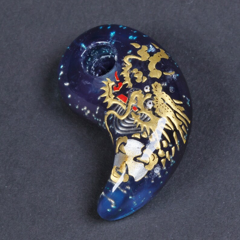 May include: A dark blue and gold dragon pendant with a hole for a cord. The pendant is made of glass and has a sparkly finish.