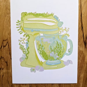 May include: A yellow and green kitchen mixer with a floral design. The bowl of the mixer is filled with green and white flowers.