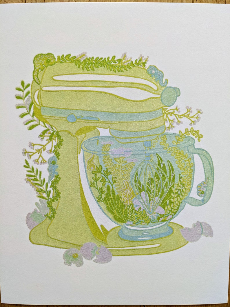 May include: A green stand mixer with a glass bowl filled with green and yellow floral designs. The mixer is decorated with green leaves and white flowers.