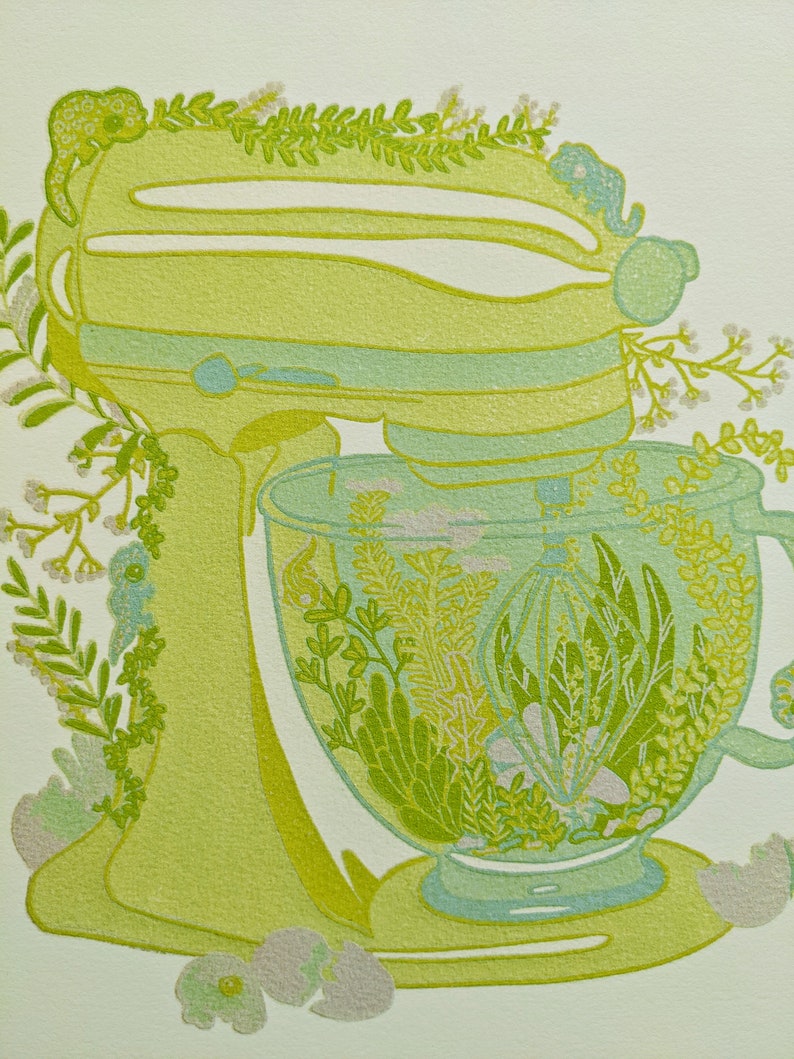 May include: A green stand mixer with a glass bowl filled with green and white floral designs. The mixer is decorated with green leaves and white flowers.