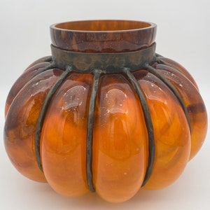 May include: Orange glass pumpkin-shaped vase with a metal cage around the top.