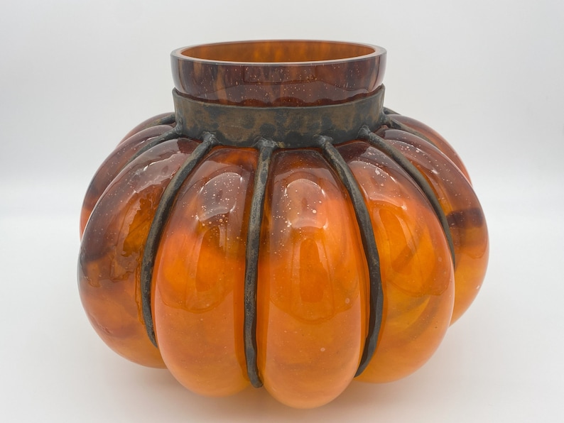 May include: Orange glass pumpkin-shaped vase with a metal cage around the top.