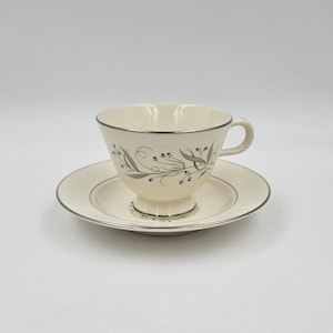 Puede incluir: Juego de taza y platillo color crema con ribete plateado. La taza presenta un delicado diseño floral en gris y verde azulado. El platillo tiene un ribete plateado a juego, creando un aspecto cohesivo y elegante. Un clásico para cualquier juego de té.