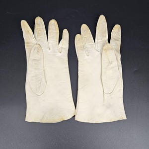 May include: A pair of off-white leather gloves. The gloves are made of a soft, supple leather and have a classic design.