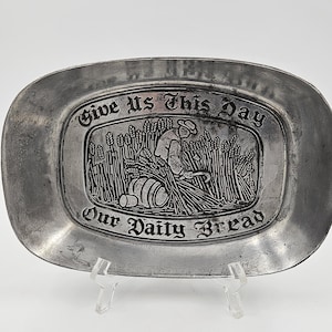 May include: A silver metal bread tray with a raised design of a person harvesting wheat. The tray reads "Give Us This Day Our Daily Bread".