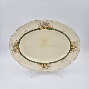 May include: An oval, off-white serving platter with a scalloped edge and a gold rim. The platter is decorated with a green border and yellow floral accents. The platter is approximately 16 inches long.