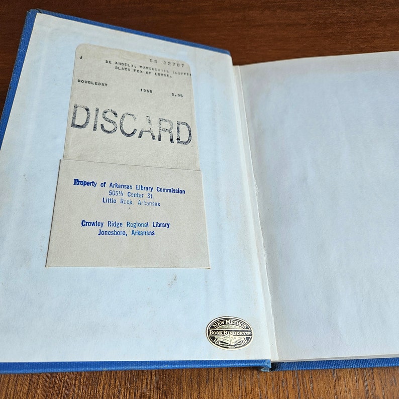 May include: A close-up of a book with a white cover and blue binding. The book has a label that says "Property of Arkansas Library Commission 505&frac12; Center St. Little Rock, Arkansas Crowley Ridge Regional Library Jonesboro, Arkansas". The book also has a stamp that says "New Method Book Bindery".