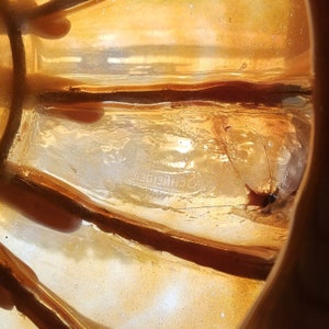 May include: Close-up of the bottom of a gold-colored glass bowl with the word "SCHNEIDER" etched into the glass.