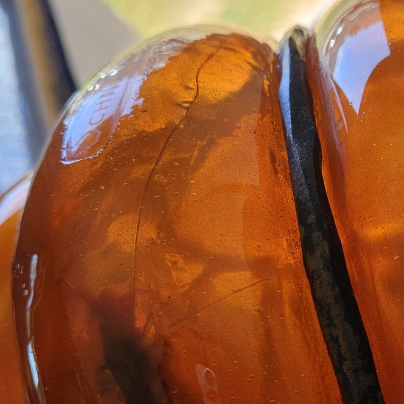 May include: Close-up of a clear amber glass bottle with a black rubber seal. The bottle has a textured surface and the text "CH" is visible on the side.