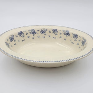 Op de afbeelding: Een witte keramische kom met een blauw bloemenpatroon rond de rand. De kom is ondiep en heeft een licht afgeronde vorm.