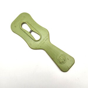 May include: A green plastic scissors sharpener with a handle and a slot for sharpening blades. The text "SCISSORS SHARPENER" is printed at the top, and "PUSH FORWARD ONLY USE THIS SIDE" is printed on the side. A lion's head is embossed on the handle.