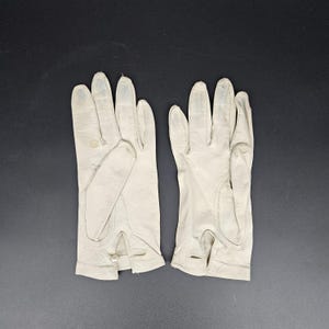 May include: A pair of white leather gloves. The gloves are long and have a button closure at the wrist.