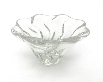 May include: A clear glass bowl featuring a wavy, organic rim and a tapered base. The transparent material has a smooth, reflective surface with subtle vertical indentations that create a flowing, petal-like appearance throughout the structure.