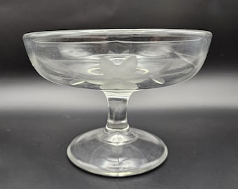 May include: A clear glass pedestal bowl with an etched floral design. The bowl has a wide, round base and a tall, slender stem.