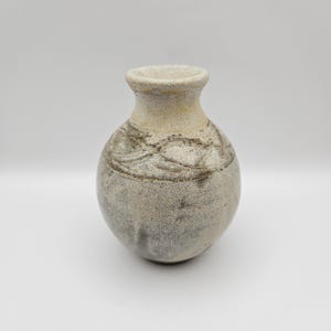 Op de afbeelding: Een kleine, ronde, grijze en witte keramische vaas met een getextureerd oppervlak en een gesneden ontwerp.