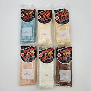 May include: Six balls of Red Heart Bulky Rug Yarn in a variety of colours, including antique blue, natural, cream, flesh tone, white, and spice. Each ball contains 320 pieces and is labelled with the colour name and number.