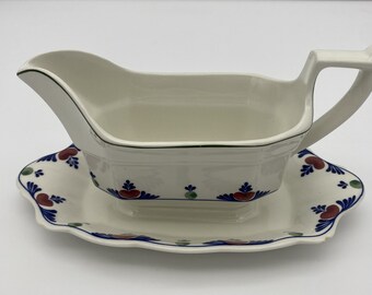 Może przedstawiać: Biała ceramiczna sosjerka z zielonym i niebieskim wzorem kwiatowym. Sosjerka stoi na pasującej podstawce.