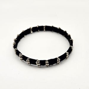 Op de afbeelding: Zwarte armband met zilverkleurige decoratieve kralen. De armband is gemaakt van een zwart, fluwelig materiaal en heeft gelijkmatig verdeelde, kleine, ronde kralen. Het ontwerp is eenvoudig en elegant, geschikt voor dagelijks gebruik.