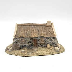 May include: A miniature stone cottage with a thatched roof. The cottage features a wooden door, small windows, and a chimney. The base includes small rocks and a barrel. The overall color palette is neutral with shades of gray, brown, and beige.