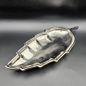 May include: A silver leaf-shaped serving tray with a decorative design. The tray has a slightly curved shape and a raised edge.