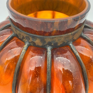 May include: Orange glass pumpkin-shaped vase with a metal cage around it. The vase has a textured surface and a shiny finish.