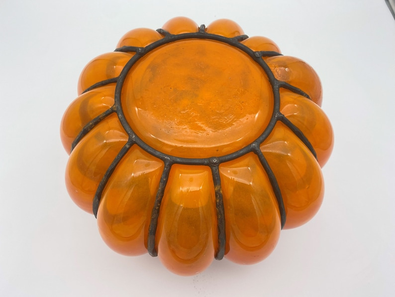 May include: Orange glass pumpkin-shaped bowl with a black metal wire frame.