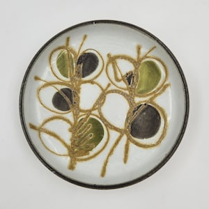 Op de afbeelding: Een ronde keramische plaat met een witte binnenkant en een donkerbruine rand. De plaat heeft een gestileerd botanisch ontwerp in bruin, groen en zwart. Het ontwerp omvat bladvormige vormen en gebogen lijnen.