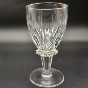 May include: A clear glass wine glass with a cut crystal design and a short stem. The glass has a wide bowl and a round base.