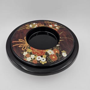Könnte beinhalten: Ein schwarzes Lacktablett mit floralem Design. Das Tablett hat einen erhöhten Rand und ein kleineres inneres Tablett. Das Blumenmuster zeigt rote, weiße und goldene Blumen auf braunem Hintergrund.