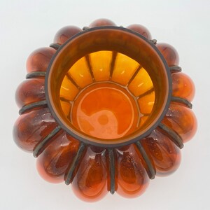 May include: A large amber glass bowl with a unique design. The bowl is shaped like a flower with multiple rounded petals. The inside of the bowl is also amber glass and has a grid pattern.