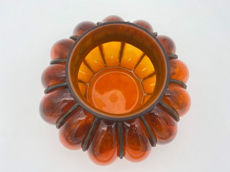 May include: A large amber glass bowl with a unique design. The bowl is shaped like a flower with multiple rounded petals. The inside of the bowl is also amber glass and has a grid pattern.