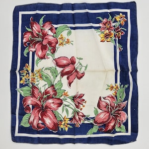 May include: Square white handkerchief with a navy blue border and floral design. The handkerchief features large red lilies, green leaves, and smaller yellow and orange flowers. The border has two navy blue stripes.