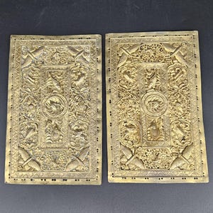 May include: Two antique gold-colored metal panels with intricate embossed floral and bird designs. The panels are rectangular and have a raised border.