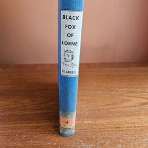 May include: A blue hardback book with the title "Black Fox of Lorne" by De Angeli. The book cover features a black and white illustration of a man wearing a crown.