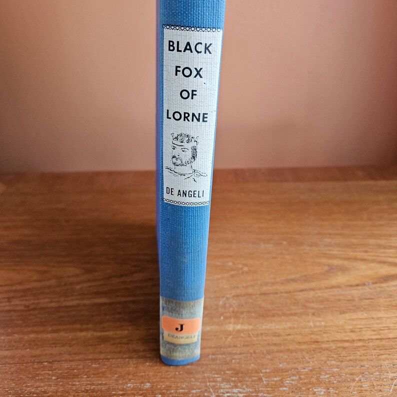 May include: A blue hardback book with the title "Black Fox of Lorne" by De Angeli. The book cover features a black and white illustration of a man wearing a crown.