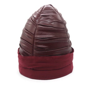 May include: A burgundy faux leather beanie with a pleated design and a matching burgundy band.