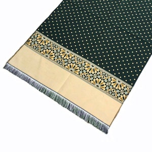 May include: A dark green prayer rug with a white polka dot pattern. The rug has a cream-colored border with a gold and black geometric design and fringe. A black beaded tasbih rests on the rug.
