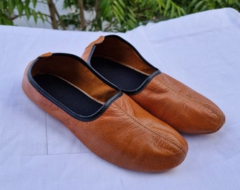 May include: A pair of brown leather slip-on shoes with black trim. The shoes are on a white surface.