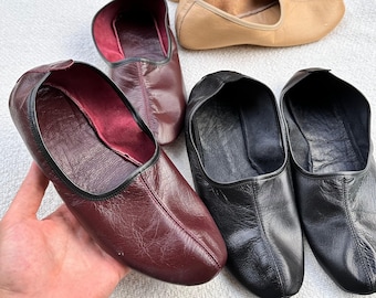 May include: Five pairs of leather slippers in various colors, including burgundy, black, and beige. The slippers have a pointed toe and a flat sole.