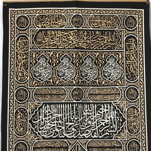 May include: Black fabric with gold and silver embroidery depicting Islamic calligraphy. The fabric features intricate patterns and designs.