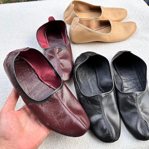 Puede incluir: Cuatro pares de zapatillas de cuero en diferentes colores. Dos pares son negros, un par es burdeos y un par es beige.