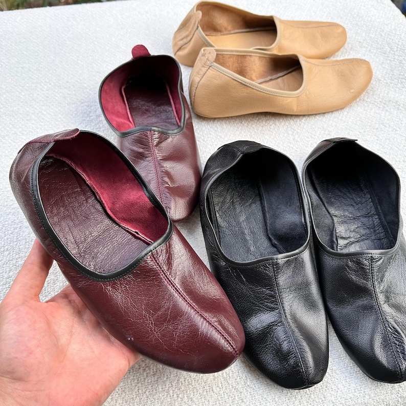 Puede incluir: Cuatro pares de zapatillas de cuero en diferentes colores. Dos pares son negros, un par es burdeos y un par es beige.