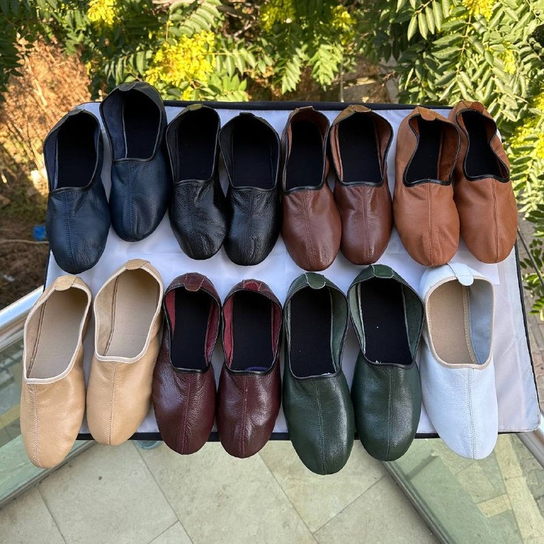 May include: A collection of 14 leather shoes in various colors, including black, brown, beige, green, and burgundy. The shoes are arranged in two rows on a white surface.