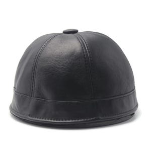 Puede incluir: Gorra de cuero negro con una corona redondeada y un pequeño botón circular en la parte superior. La gorra tiene una visera corta y curvada y está hecha de cuero liso y brillante. La gorra es de color negro liso y es probablemente un accesorio de moda.