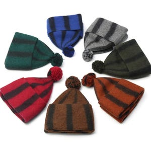 Puede incluir: Siete gorros de punto a rayas con pompones en varios colores, incluyendo rojo, verde, azul, marrón y gris.