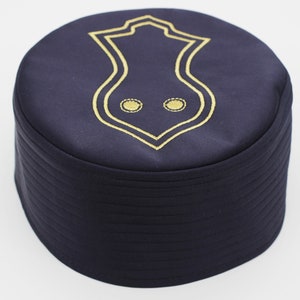 Könnte beinhalten: Eine dunkelblaue Mütze mit einem goldenen Stickmuster. Das Muster zeigt eine stilisierte Form mit zwei Kreisen darin.