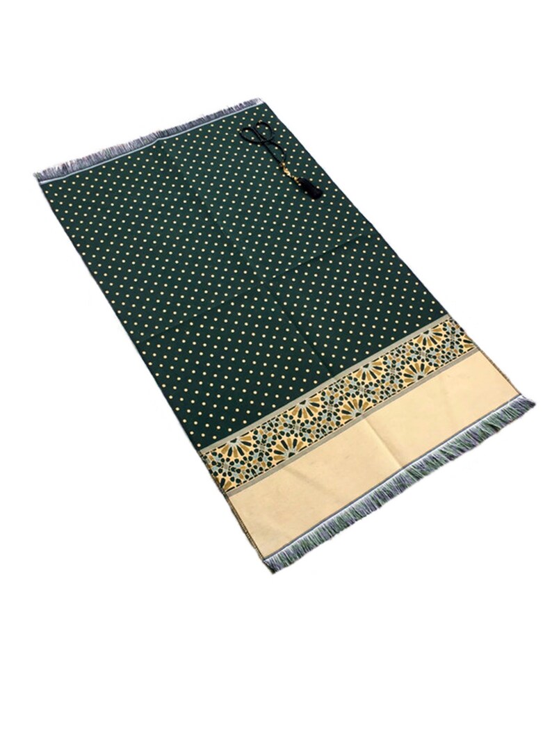 May include: A dark green prayer rug with a repeating pattern of small, light-colored dots. The rug has a decorative border with geometric designs in gold and tan, and a fringed edge. A set of prayer beads rests on the rug.