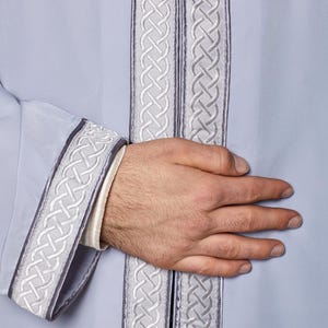 May include: A light blue robe with a white and grey braided trim. The trim is on the sleeves, collar, and front of the robe.