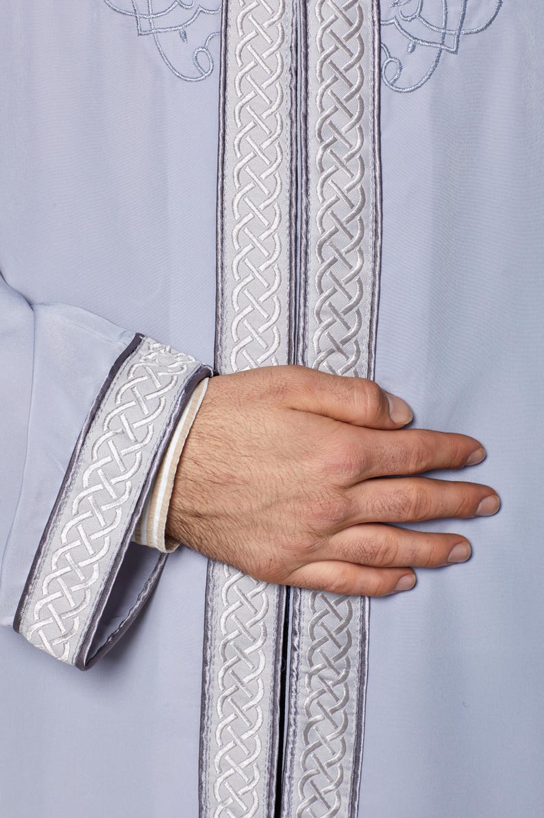 May include: A light blue robe with a white and grey braided trim. The trim is on the sleeves, collar, and front of the robe.