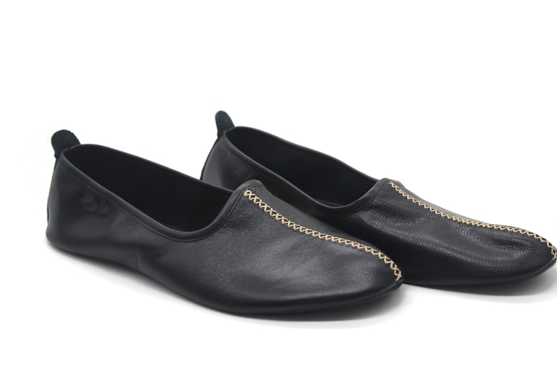 Puede incluir: Par de zapatos negros de cuero con detalles de costuras doradas.